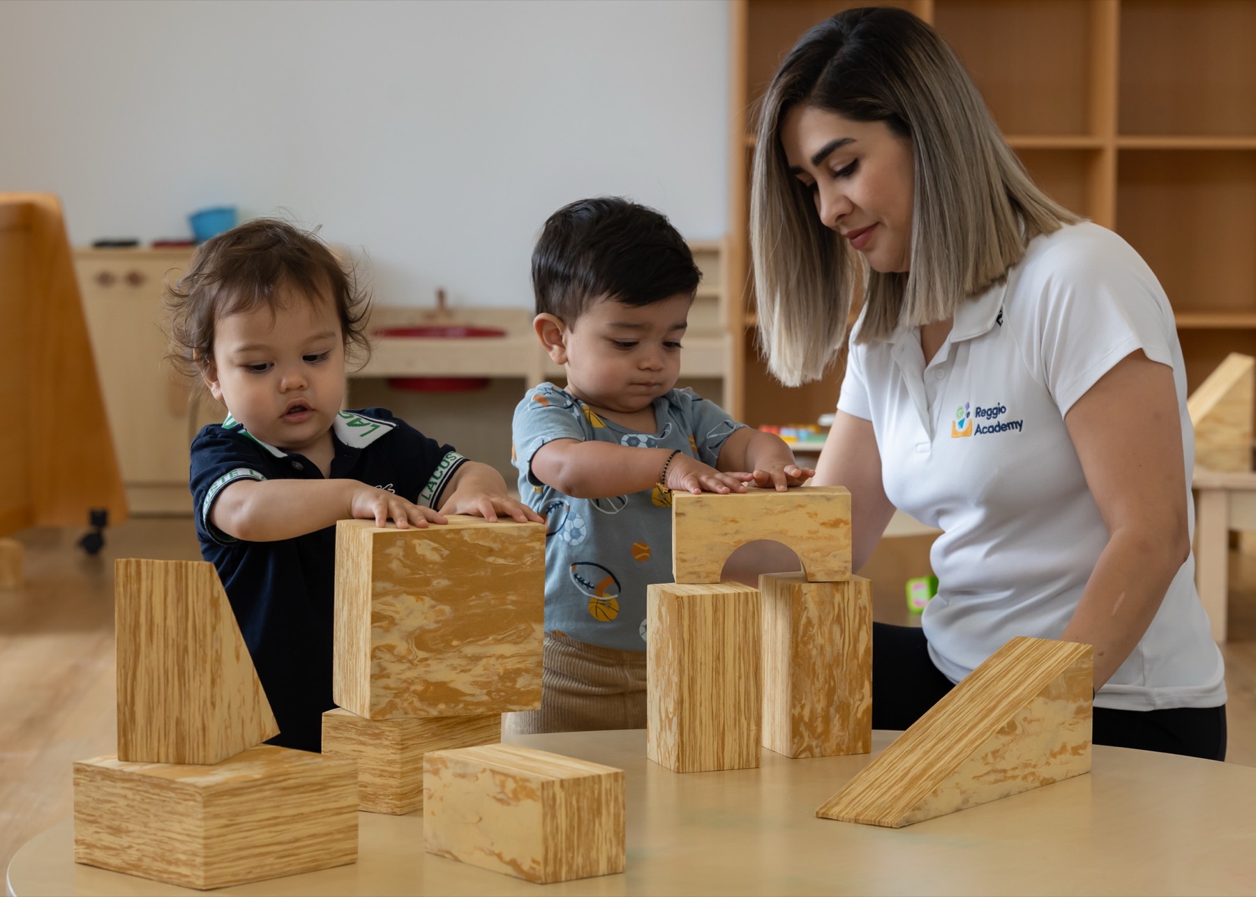 An educator building with timber blocks alongside two toddlers