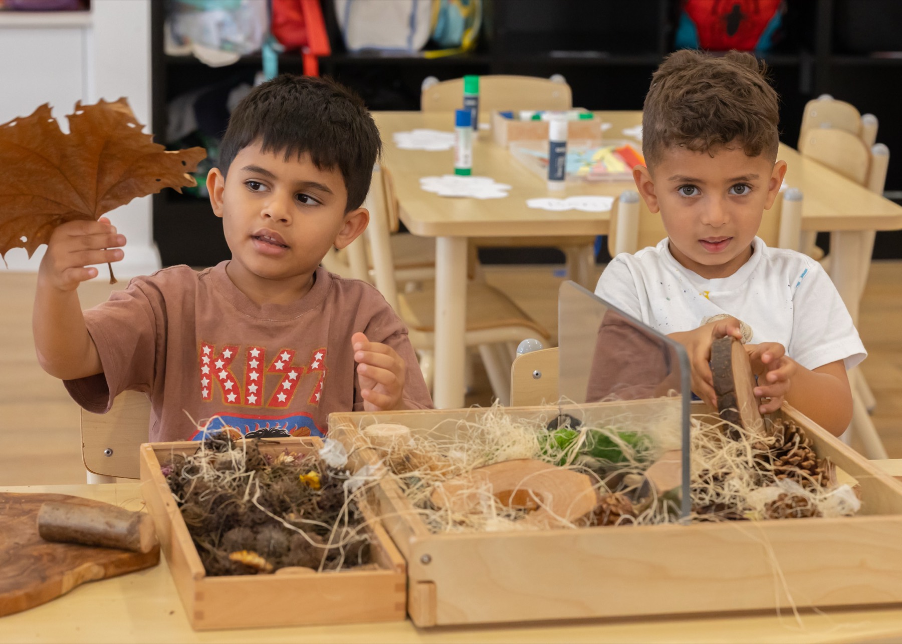 Children exploring leaves and natural materials in timber trays