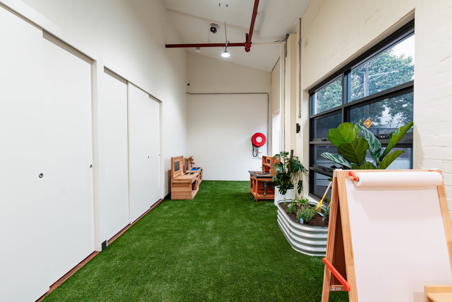 An indoor green play space with an easel and planter boxes
